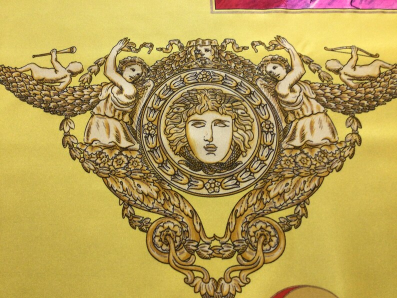 Puede incluir: Una tela amarilla con un dise&ntilde;o dorado ornamentado. El dise&ntilde;o presenta un medall&oacute;n central con un rostro, flanqueado por figuras y querubines. La est&eacute;tica general es cl&aacute;sica y decorativa.