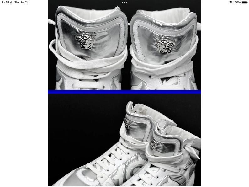 May include: High-top white sneakers with silver accents. The sneakers feature a silver panel on the upper and a Medusa head emblem. White laces and a padded collar complete the design. The shoes are set against a black background.
