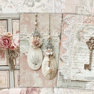May include: A collage featuring vintage-style elements. It includes a small chest of drawers, keys, floral arrangements, and decorative oval pendants with floral and pearl accents. The color palette is soft, with pinks, creams, and touches of gold.