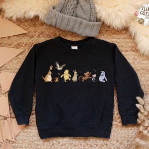 May include: Black sweatshirt with a Winnie the Pooh and friends graphic print. The print features Winnie the Pooh, Piglet, Tigger, Eeyore, Kanga, Roo, and a bird. The sweatshirt has a crew neck and long sleeves.