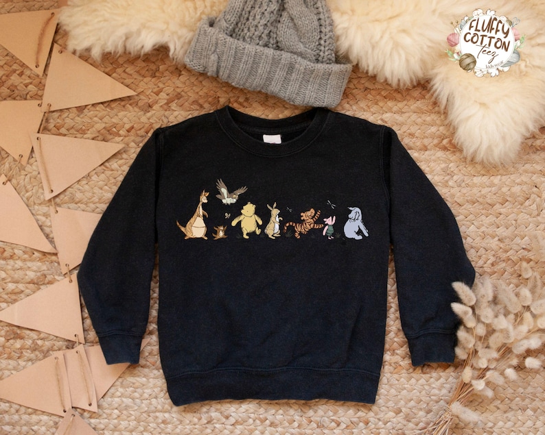 May include: Black sweatshirt with a Winnie the Pooh and friends graphic print. The print features Winnie the Pooh, Piglet, Tigger, Eeyore, Kanga, Roo, and a bird. The sweatshirt has a crew neck and long sleeves.
