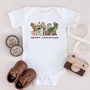May include: White baby onesie with a Christmas-themed image of the Toy Story characters, including Woody, Buzz Lightyear, and Rex. The text "Merry Christmas" is printed below the image.