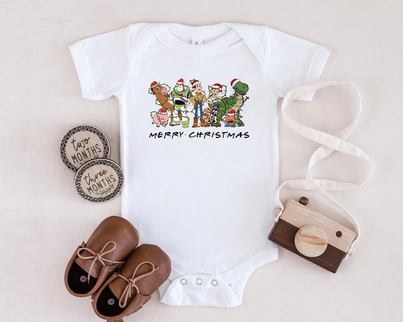 May include: White baby onesie with a Christmas-themed image of the Toy Story characters, including Woody, Buzz Lightyear, and Rex. The text "Merry Christmas" is printed below the image.