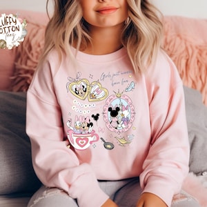 Puede incluir: Sudadera rosa claro con personajes de Disney, Minnie y Daisy. El dise&ntilde;o gr&aacute;fico incluye el texto "Girls just wanna have fun". El dise&ntilde;o incorpora corazones, coronas y otros elementos decorativos.