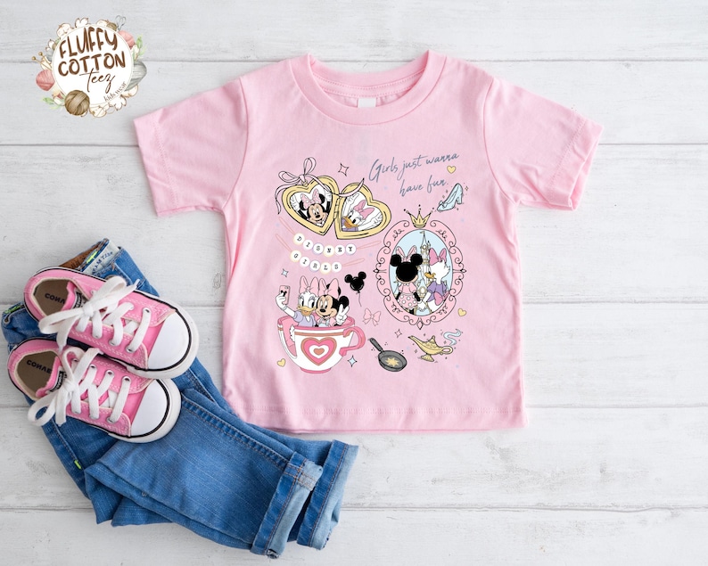 Puede incluir: Camiseta rosa de manga corta con un dise&ntilde;o de Minnie y Daisy Duck. El dise&ntilde;o incluye corazones, una taza de t&eacute; y el texto "Girls just wanna have fun". Zapatillas rosas y vaqueros azules tambi&eacute;n en la imagen.