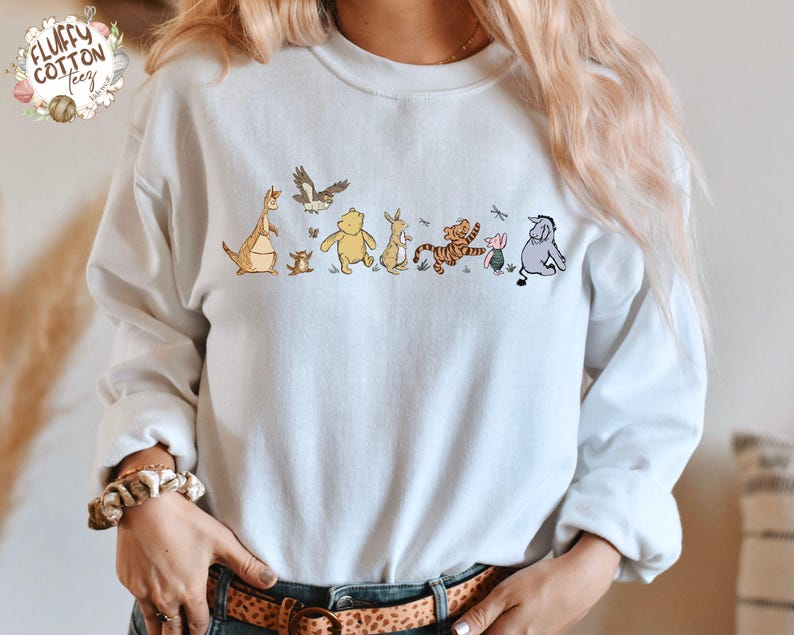 May include: A light blue sweatshirt with a graphic of Winnie the Pooh and his friends. The characters are in a line, walking from left to right. The characters include Tigger, Piglet, Eeyore, Kanga, Roo, and Rabbit.