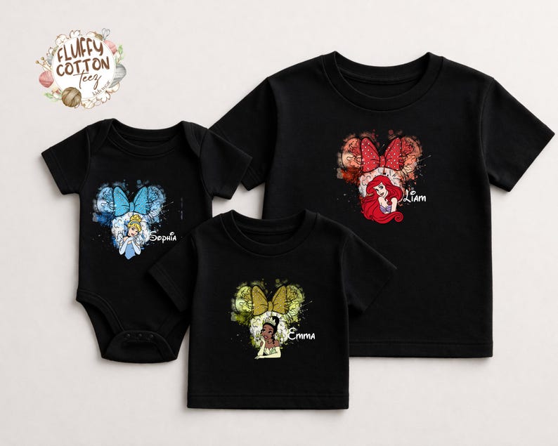 以下が含まれることがあります： 黒いTシャツと、ディズニーのプリンセスデザインのボディスーツ。シンデレラ、アリエル、ティアナのデザインで、それぞれミッキーマウスの耳の形をした水彩画のスプラッシュの中に描かれています。キャラクターの下には名前が印刷されています。「Fluffy Cotton Teez」のブランドロゴが左上にあります。