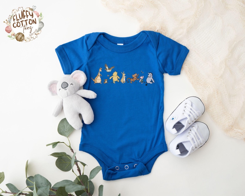 May include: A royal blue baby onesie with a graphic of characters from the movie 'The Lion King'. The characters include Simba, Timon, Pumbaa, and Zazu. The onesie has short sleeves and a snap closure.