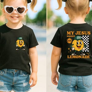 K&ouml;nnte beinhalten: Schwarzes Kurzarm-T-Shirt mit einem Cartoon-Zitronen-Motiv auf der Vorder- und R&uuml;ckseite. Auf der Vorderseite ist eine Zitrone mit Hut abgebildet. Auf der R&uuml;ckseite des Shirts steht "MY JESUS MAKES LEMONADE".