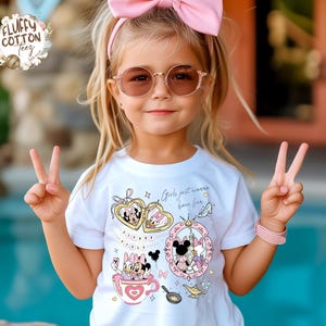 Puede incluir: Una camiseta blanca con gr&aacute;ficos coloridos de personajes de Disney, incluyendo a Minnie y Daisy, y el texto "Girls just wanna have fun." La camiseta la lleva una persona joven con una diadema rosa y gafas de sol.