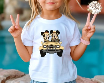May include: White t-shirt featuring a cartoon image of Mickey and Minnie Mouse in a yellow jeep. The cartoon characters are wearing safari hats and driving a yellow jeep. The shirt is being worn by a child.