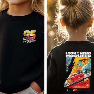 May include: Black sweatshirt with Lightning McQueen and the number 95. The front has a small graphic with "Lightning McQueen" and the number 95. The back features a larger graphic with "LIGHTNING McQUEEN" and a Cars-themed design.