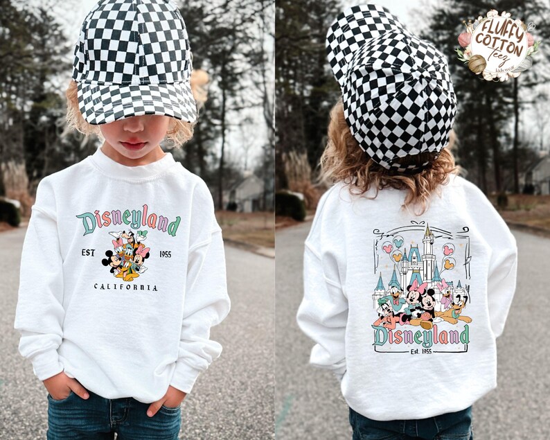 May include: A white sweatshirt with "Disneyland" in teal script and a graphic of Disney characters. The front of the shirt has the text "EST 1955 CALIFORNIA". The child is wearing a black and white checkered baseball cap.