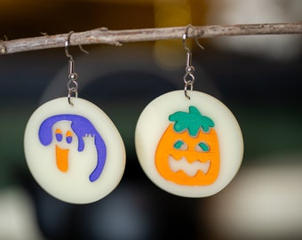 Könnte beinhalten: Ein Paar Halloween-Ohrringe. Ein Ohrring zeigt einen weißen Geist mit violetten und orangefarbenen Details. Der andere Ohrring zeigt einen weißen Kürbis mit orangefarbenen, grünen und weißen Details.