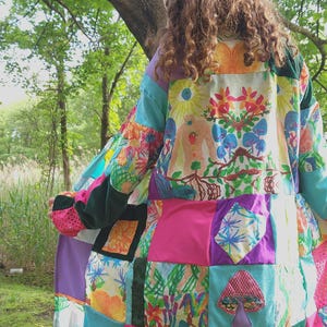 May include: A colorful patchwork coat with a whimsical design. The coat features a variety of fabric squares in shades of pink, blue, green, and purple, with floral and mushroom appliqués. The coat is worn outdoors, with a blurred background of trees.