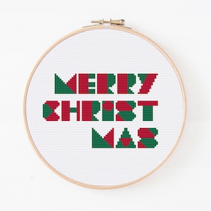 May include: A white embroidery hoop with a cross-stitch design that reads "Merry Christmas" in red and green. The letters are made up of geometric shapes.