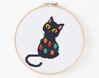 May include: A black cat with yellow eyes and pink ears is wrapped in colorful Christmas lights. The cat is sitting on a white background.