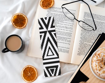 Peut inclure: Un marque-page en perles géométriques noir et blanc est placé dans un livre ouvert avec des lunettes de lecture, une tasse de café, des tranches d'orange séchées et un beignet sur une planche à découper en bois.