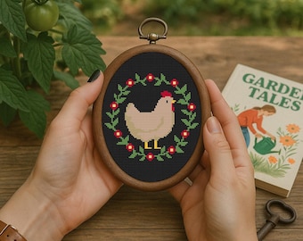 May include: A wooden framed embroidery hoop with a white chicken with a red comb and a black background. The chicken is surrounded by a wreath of green leaves and red flowers.