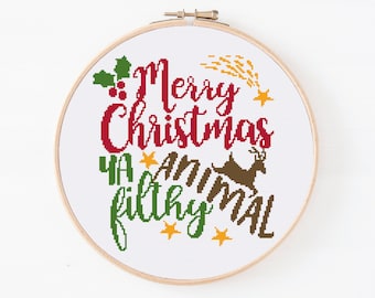 May include: Cross stitch pattern with the text "Merry Christmas Ya Filthy Animal" in red, green, and brown lettering. There are also yellow stars and a brown reindeer.