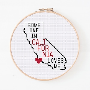 May include: A white embroidery hoop with a black outline of the state of California. The text "Some one in Cali for Nia loves me" is written inside the outline. A red heart is placed in the center of the state.