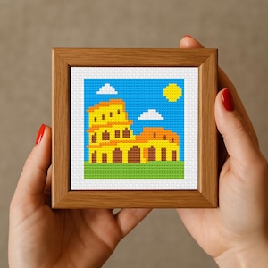 May include: A cross-stitch pattern of the Colosseum in Rome, Italy. The Colosseum is yellow with brown arches and is set against a blue sky with white clouds and a yellow sun.