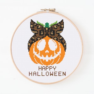 May include: Cross stitch pattern of a pumpkin with a leopard print bandana and the text "Happy Halloween".