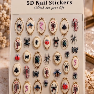 May include: A sheet of CoCo Notes 5D nail stickers featuring various insects and arachnids, including scorpions, spiders, beetles, and butterflies. Many designs are encased in ornate gold-toned oval frames on a cream-colored backing card.