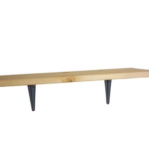 Puede incluir: Estantería flotante de madera clara con dos soportes metálicos de color gris oscuro. La estantería parece inacabada. Los soportes son triangulares y sostienen la estantería. La longitud es de unos 120 cm.