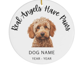 May include: White ceramic ornament with a brown and gold doodle dog. The ornament reads "Real Angels Have Paws" and has space for a dog's name and dates.