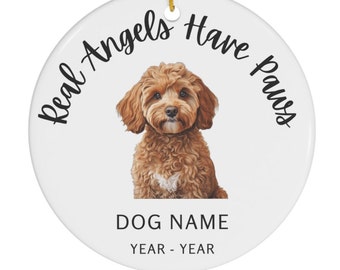 May include: White ceramic ornament with a brown and white dog illustration. The text "Real Angels Have Paws" is written in a black cursive font around the dog. The text "DOG NAME" and "YEAR - YEAR" is written in black below the dog.