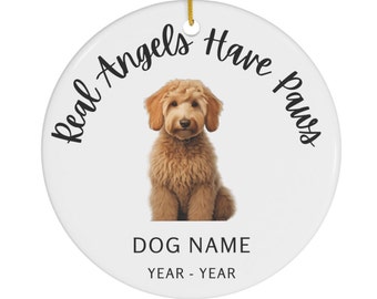 May include: White ceramic ornament with a brown and white dog sitting in the center. The text "Real Angels Have Paws" is written in a circle around the dog. Below the dog is the text "DOG NAME YEAR - YEAR".