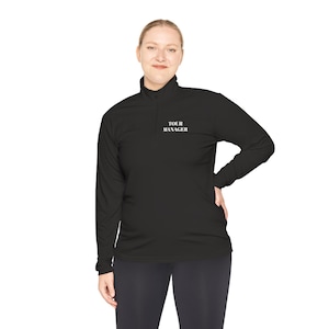 May include: Black long-sleeve shirt with a mock neck and a zipper. The shirt has the text "TOUR MANAGER" embroidered on the chest.