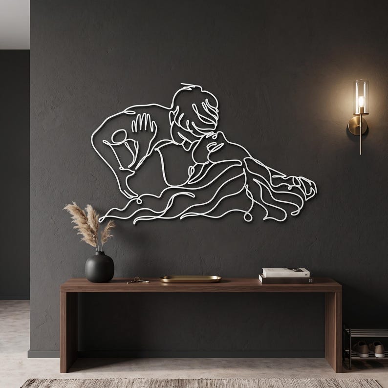 Elegant entryway metal wall art depicting a romantic couple in a crisp white finish, mounted above a dark wood modern console table with decor.