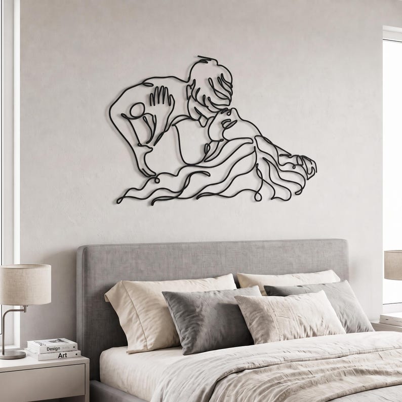 Minimalist metal wall art of a kissing couple in a matte black finish, centered perfectly above a grey upholstered bed in a bright modern bedroom.