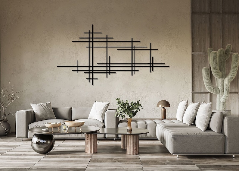 Puede incluir: Un sal&oacute;n moderno con un sof&aacute; seccional gris, una mesa de caf&eacute; con dos cuencos y una escultura de pared de metal negro. La habitaci&oacute;n tiene un suelo de madera marr&oacute;n claro y una pared beige.