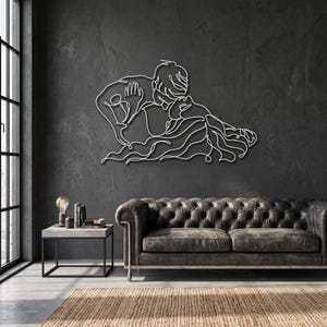 Modern metal wall art featuring a romantic line art couple embrace, finished in silver and hanging above a leather sofa in an industrial living room.