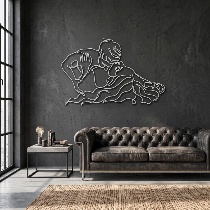 Modern metal wall art featuring a romantic line art couple embrace, finished in silver and hanging above a leather sofa in an industrial living room.