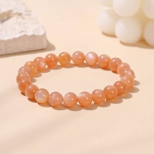 Puede incluir: Un brazalete hecho de cuentas de piedra de sol naranja. Las cuentas son redondas y tienen un acabado liso y pulido.
