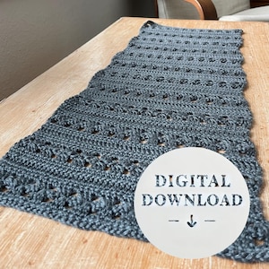 Può includere: Un runner da tavolo in crochet grigio con un motivo traforato. Il testo "DIGITAL DOWNLOAD" è stampato su un cerchio bianco.