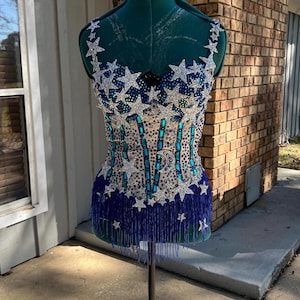 May include: A blue and silver sequined bodice with a star pattern and blue fringe. The bodice is on a mannequin.