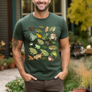May include: A dark green t-shirt with a pattern of frogs in various colors and poses. The frogs are green, brown, yellow, and white.