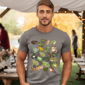 May include: A gray t-shirt with a pattern of various frogs in different colors and poses. The frogs are green, brown, yellow, and orange.