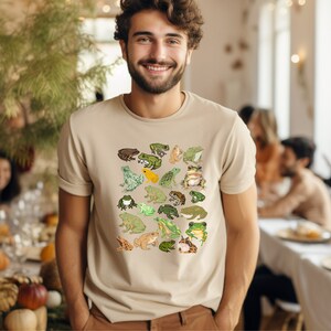 May include: A beige t-shirt with a pattern of green, brown, and yellow frogs. The frogs are arranged in a grid pattern on the front of the shirt.