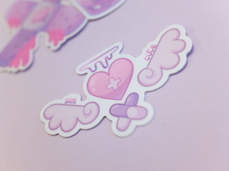 May include: A sticker featuring a pink heart with a cross, angel wings, and a halo. The sticker has the words "sick" and "cute" on it. The colour palette includes light pink, purple, and white. The design is whimsical and cute.