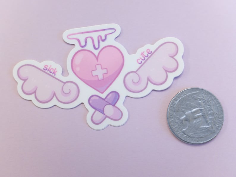 May include: A sticker featuring a pink heart with a cross, wings, and pills. The heart has a dripping design at the top. The words "sick" and "cute" are on the wings. A coin is next to the sticker.