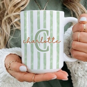 May include: White ceramic mug with green vertical stripes and the name "Charlotte" in a cursive font. The letter "C" is in a larger, green font. The mug has a white handle.
