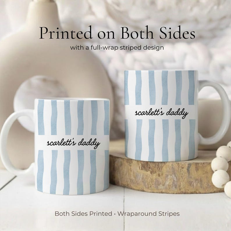 Puede incluir: Dos tazas de cer&aacute;mica blancas con rayas verticales azules y el texto "scarlett's daddy". Las tazas tienen un dise&ntilde;o de rayas envolventes y est&aacute;n impresas por ambas caras. Las tazas est&aacute;n sobre una superficie de madera.