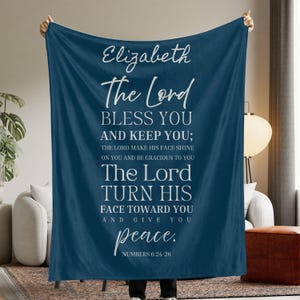 May include: A navy blue blanket with white text. The text includes the name "Elizabeth" and a passage from Numbers 6:24-26, offering blessings and peace. The blanket is held up, showcasing the design.