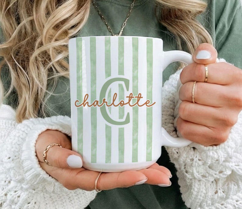 May include: White ceramic mug with green vertical stripes and the name "Charlotte" in a cursive font. The letter "C" is in a larger, green font. The mug has a white handle.